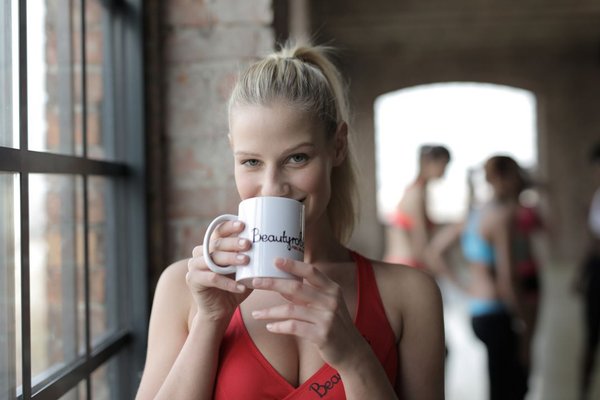 Frau die Tee als Sportgetränk für Sportler aus einer Tasse trinkt.