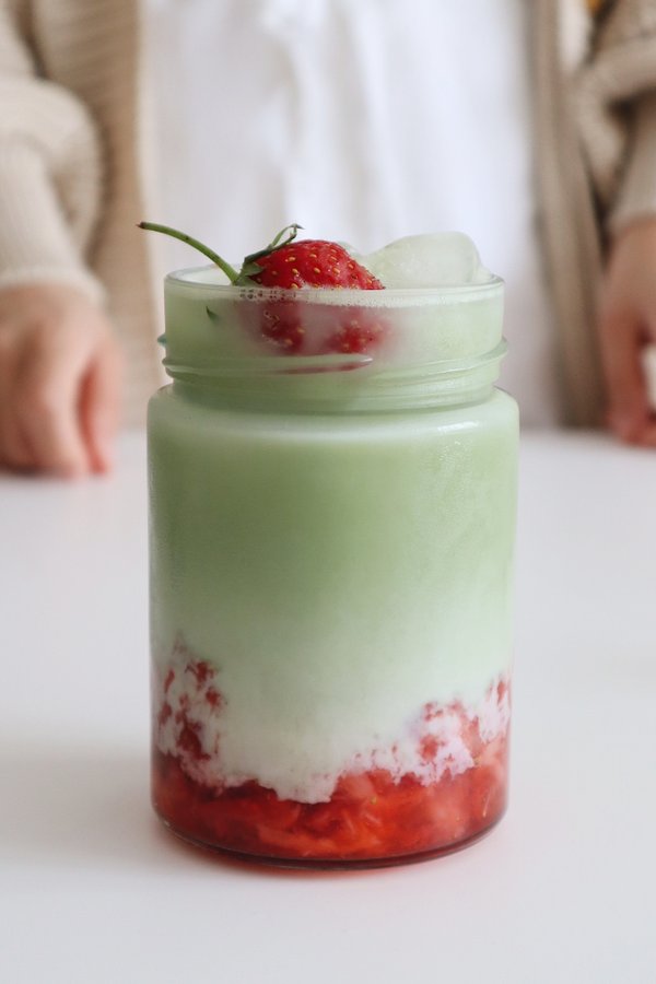 Matcha Latte in einem Glas mit Erdbeeren.