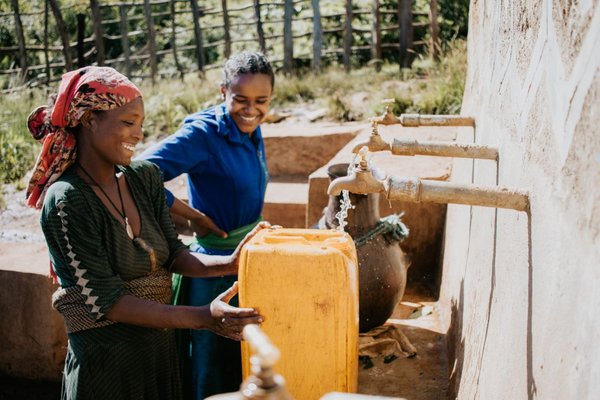 Frauen die an einem Brunnen Wasser abfüllen.
